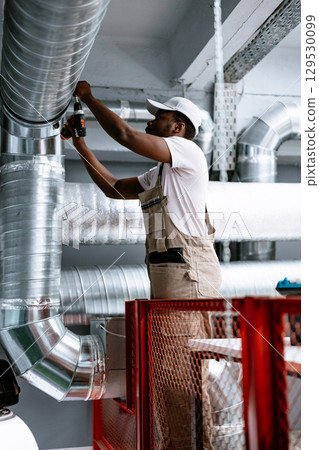 Skilled worker installing ventilation pipes in modern facility during daylight hours 129530099