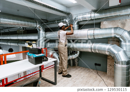 Skilled worker installing ventilation system in modern commercial building during daytime 129530115