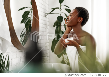 Woman applying skincare in a bright bathroom filled with plants during a morning routine 129530177