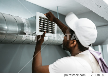 Worker installing air duct vent in a residential basement during the day Worker installing air duct vent in a residential basement during the day 129530180