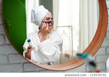 Woman applying facial mask in a cozy bathroom while practicing self-care in the morning 129530192