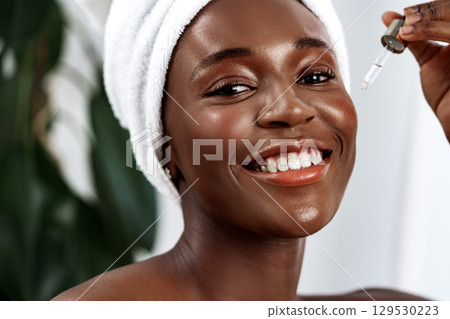 Woman applying serum to her skin with a joyful smile in a bright indoor setting 129530223