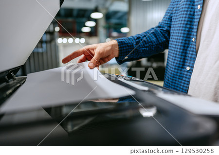 Person using a copier to scan documents in a modern office environment during the day 129530258