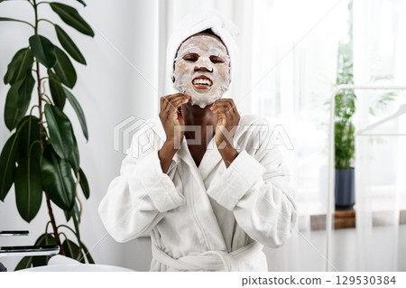 Woman enjoying a facial treatment at home while smiling in a cozy bathroom setting Woman enjoying a facial treatment at home while smiling in a cozy bathroom setting 129530384