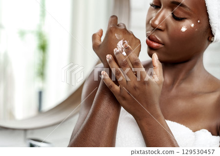 Young woman applying moisturizer to her arm in a bright bathroom during personal care routine 129530457