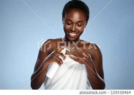 Smiling woman applying moisturizer in a bright, serene setting during a skincare routine 129530464