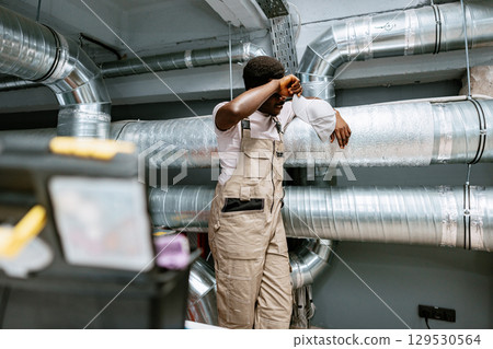 Worker takes a break beside ventilation ducts in an industrial setting during the afternoon 129530564