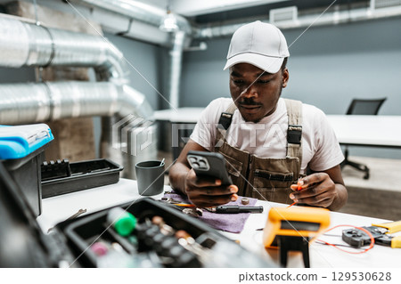 Technician working on a smartphone while seated at a desk in a modern workspace during daytime Technician working on a smartphone while seated at a desk in a modern workspace during daytime 129530628