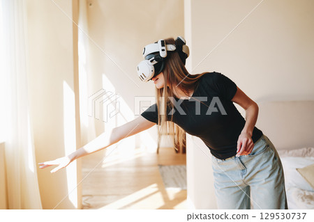 Young woman engages in virtual reality experience in a bright and modern indoor space while exploring interactive elements 129530737