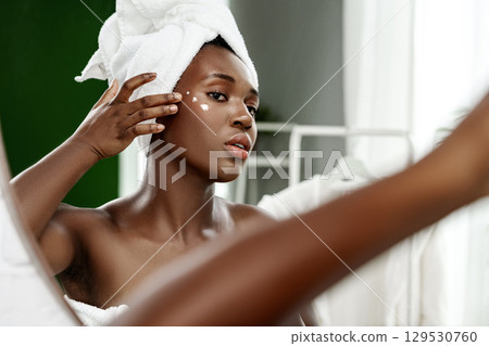 Woman applying skincare product in a bright, modern bathroom after a relaxing shower 129530760