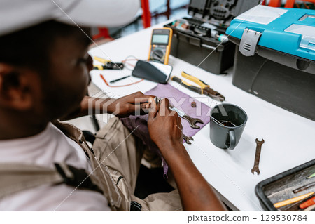 Technician repairs tools in workshop while sitting at desk with various instruments and materials Technician repairs tools in workshop while sitting at desk with various instruments and materials 129530784