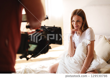 Model poses playfully during a photoshoot session in a sunlit bedroom setting with soft bedding 129530786
