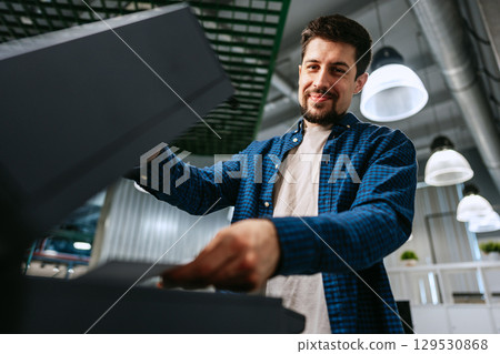 Man efficiently using a printer in a modern office environment during daytime hours 129530868