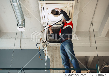 Technician repairing an air conditioning unit in a modern indoor setting during evening hours Technician repairing an air conditioning unit in a modern indoor setting during evening hours 129530874