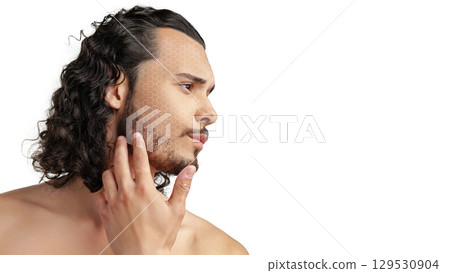 Man with curly hair touching his jawline while looking thoughtfully to the side in a minimalist setting 129530904