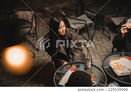 Group of friends enjoying food and drink outside at night in a cozy atmosphere Group of friends enjoying food and drink outside at night in a cozy atmosphere 129530906