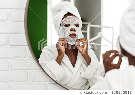 Woman applying a facial mask in a bright bathroom while looking in the mirror for self-care and relaxation Woman applying a facial mask in a bright bathroom while looking in the mirror for self-care and relaxation 129530918