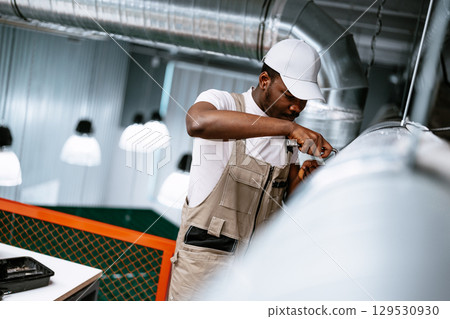 Worker performs maintenance on ventilation system in modern industrial space during daylight hours Worker performs maintenance on ventilation system in modern industrial space during daylight hours 129530930
