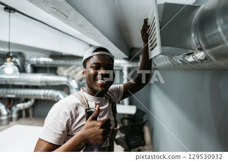 Young man smiles and gives thumbs up while hanging a notice in modern office space during daytime Young man smiles and gives thumbs up while hanging a notice in modern office space during daytime 129530932