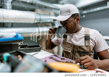 Man enjoying a warm drink while working on tools in a modern workshop setting during the day 129530941