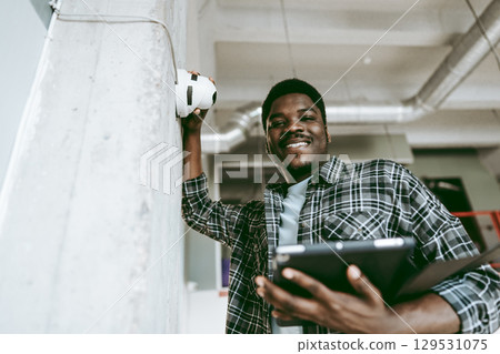Young man using tablet while smiling and leaning against wall in modern workspace Young man using tablet while smiling and leaning against wall in modern workspace 129531075