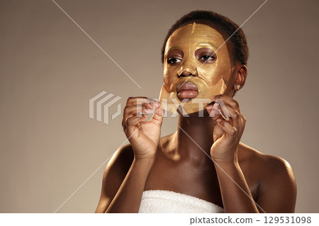 Woman applies a golden sheet mask in a skincare routine at a studio during a daytime session Woman applies a golden sheet mask in a skincare routine at a studio during a daytime session 129531098