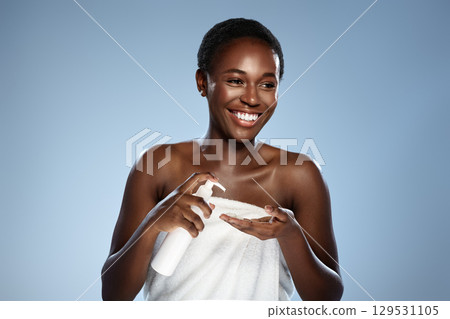Young woman applying skincare product while smiling against a light blue background in a wellness studio 129531105