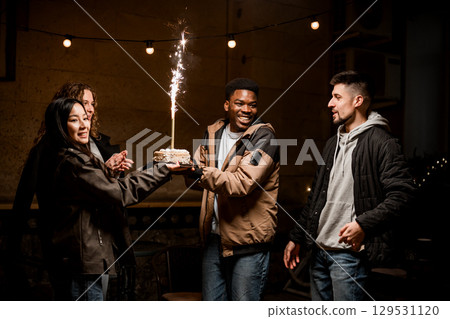 Friends celebrate with cake and sparklers in a cozy indoor gathering at night Friends celebrate with cake and sparklers in a cozy indoor gathering at night 129531120
