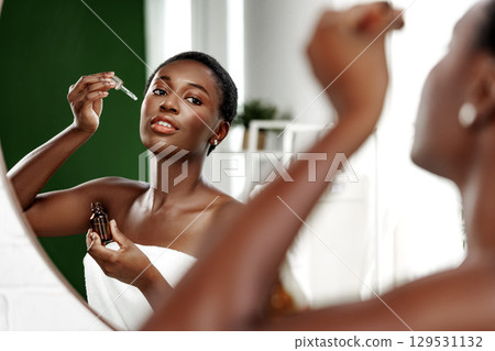 Skincare routine in bright bathroom with woman applying serum in front of mirror 129531132