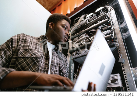 IT professional manages server rack while working on laptop in a data center during afternoon hours 129531141