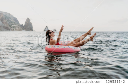 Woman floating happily in the sea on a donut ring with cliff background and copy space. 129531142