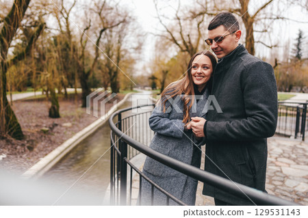 Couple enjoys a romantic moment on a bridge amidst trees in a serene park during early spring 129531143