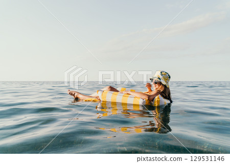 Woman Inflatable Float Sea Relaxing - A woman in a hat relaxes on an inflatable float in the sea. 129531146