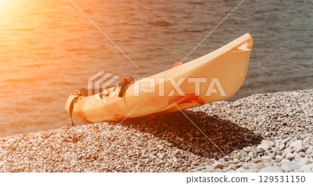 Kayak Beach Sunset - Orange kayak resting on pebbled beach at sunset. Kayak Beach Sunset - Orange kayak resting on pebbled beach at sunset. 129531150
