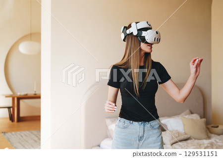 Woman experiences virtual reality in a cozy, modern bedroom during daytime 129531151