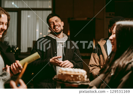 Friends celebrate together with laughter and joy during a cozy gathering at night with a cake 129531169