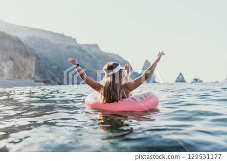 Woman floating ocean. Young woman floating on a donut ring in the sea with arms raised, enjoying summer vacation. 129531177