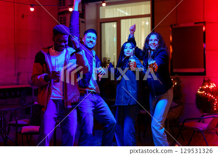 Friends celebrating together at a vibrant night gathering with drinks in hand during an outdoor party 129531326