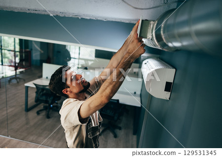 Skilled technician repairing air conditioning unit in modern office space during daytime 129531345