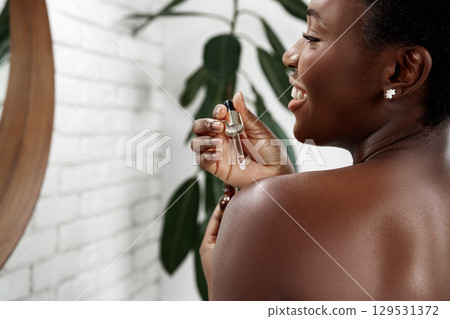 Skincare routine featuring a woman applying serum with a smile in a serene bathroom setting 129531372