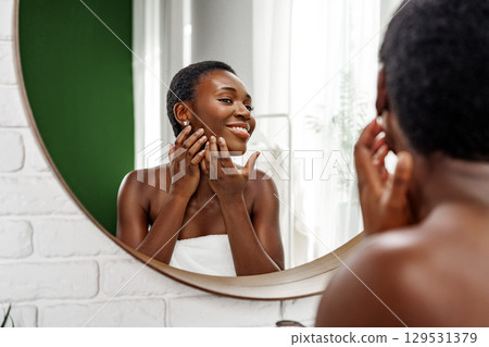Woman caring for her skin in a bright bathroom with natural lighting and a mirror reflection during the daytime Woman caring for her skin in a bright bathroom with natural lighting and a mirror reflection during the daytime 129531379