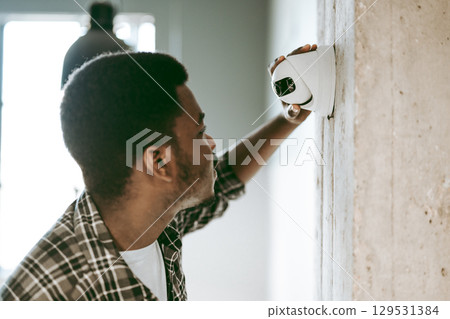 Man inspecting security camera installation in modern interior space during daylight hours Man inspecting security camera installation in modern interior space during daylight hours 129531384
