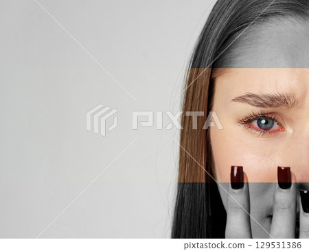 Young woman with long brown hair expressing emotion while covering half her face with her hand in a minimalist setting 129531386