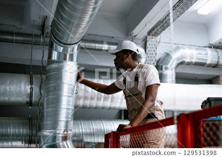 Skilled worker inspecting air ducts in a commercial building during the daytime 129531398