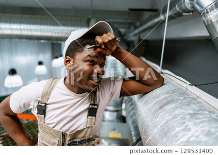 Worker assesses air duct installation in industrial space during daylight hours 129531400
