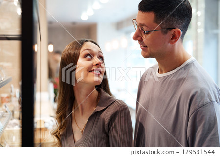 Couple enjoying conversation in modern cafe while browsing desserts on display during afternoon visit Couple enjoying conversation in modern cafe while browsing desserts on display during afternoon visit 129531544