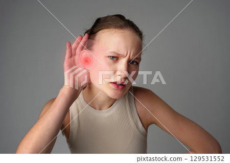Young woman experiencing ear pain and discomfort while holding her hand to her ear in a neutral setting 129531552