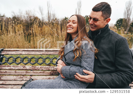 Couple enjoying a cozy moment together on a bench in a park during a chilly afternoon 129531558