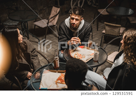 Friends enjoy late-night pizza and drinks while socializing at an outdoor cafe in the city 129531591