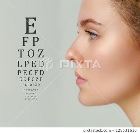 Eye examination chart displayed next to a model undergoing vision assessment in a clinical setting 129531616
